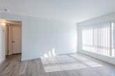 This single-floor space offers a clean, minimalist layout bathed in natural light throughout. Light wood-style flooring runs continuously across all areas, creating a cohesive and airy feel. The open living and dining area is generously sized, featuring a ceiling fan and large windows dressed with vertical blinds that allow sunlight to filter in, casting warm patterns across the floor.

The galley-style kitchen is efficiently designed with white cabinetry lining both sides, gray laminate countertops, an electric range with overhead ventilation, and a dishwasher. The crisp white cabinetry and neutral countertops lend a modern, functional quality to the space.

The bedrooms continue the bright, open aesthetic with large windows providing ample natural light and ceiling fans for added comfort. Textured ceilings add a subtle architectural detail present in several rooms.

The bathroom is neatly appointed with a white vanity featuring under-sink cabinetry, a large frameless mirror, brushed nickel fixtures, and chrome towel bars, maintaining the clean and consistent style found throughout the rest of the unit.

Overall, the space presents a light, neutral palette with a practical layout that maximizes functionality, making it a well-organized and inviting single-floor residence.