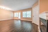 This two-floor residence offers a well-organized layout with a range of practical features throughout. The main living area is bright and open, finished with rich dark hardwood flooring and neutral-toned walls. Large windows fitted with blinds allow generous natural light to fill the space, while a glass door provides direct outdoor access. A fireplace adds a focal point to the living room, contributing to a warm and welcoming atmosphere. Track lighting overhead ensures consistent illumination throughout the open-plan area.

The kitchen is positioned adjacent to the living space and features warm wood cabinetry, dark granite countertops, and stainless steel appliances including a gas range and over-the-range microwave. A peninsula counter creates a natural separation between the kitchen and the main living area.

The bathrooms are finished with neutral beige tile work. One bathroom includes a soaking tub with full tile surround, while another offers a glass-enclosed walk-in shower with a built-in shelf and chrome fixtures.

The bedrooms are carpeted and receive natural light through windows overlooking greenery. A dedicated laundry area houses a full-sized washer and dryer tucked neatly under a stairwell. The attached garage provides additional utility with ample space for parking and storage.