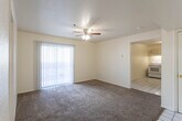 Located at 2049 S Triviz Dr in Las Cruces, New Mexico, this single-floor residence offers a straightforward and functional layout designed for comfortable everyday living. The living room serves as the heart of the home, featuring plush wall-to-wall carpeting, a ceiling fan with integrated lighting, and a full-width sliding glass door dressed with vertical blinds that invites natural light and provides direct access to the outdoors. The adjoining kitchen is efficiently arranged in an L-shaped configuration, outfitted with light wood cabinetry, ample counter space, a stainless steel sink, and white appliances including a range, dishwasher, and overhead ventilation hood. White ceramic tile flooring runs throughout the kitchen and entryway, offering a clean contrast to the carpeted rooms. The entry area features two white doors and a tiled floor, creating a welcoming transition into the home. The bedrooms are generously proportioned, each finished with soft carpeting and windows fitted with blinds that allow for natural light while maintaining privacy. The bathroom includes a full tub-shower combination, a vanity with light wood cabinetry, and white tile flooring. Throughout the space, neutral wall tones and consistent finishes contribute to a clean, cohesive aesthetic.