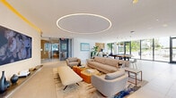 Located at 201 Clearwater Dr in West Palm Beach, FL, this elegantly designed amenity lounge spans a generous single floor and is thoughtfully divided into two distinct living areas. The space makes an immediate impression with its signature oversized circular LED ceiling fixture, which anchors the main lounge and casts a warm, ambient glow across the open-plan layout. Large-format porcelain tile flooring runs throughout, lending a clean, cohesive aesthetic.

The primary living area features a curated arrangement of contemporary seating, oriented around warm wood coffee tables, with floor-to-ceiling windows along the perimeter that flood the space with natural light and offer views of the surrounding outdoor greenery. A wall-mounted display and a floating media console provide a refined focal point.

Adjacent areas include a game room with a billiards table, a dining zone with a sculptural marble-topped table set against a richly textured woven wood accent wall, and a conference-style room enclosed by sleek steel-framed glass partitions. A separate lounge zone features a bold blue accent wall, built-in cabinetry, and a conference table — ideal for private gatherings.

An outdoor terrace, accessible through sliding glass doors, extends the living space further, offering a sectional seating area backed by the same distinctive woven wood wall texture seen indoors.