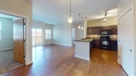 This single-floor residence offers a thoughtfully designed open-concept layout that seamlessly connects the living area and kitchen. Rich hardwood flooring extends throughout the main living space, complemented by neutral-toned walls that create a bright, welcoming atmosphere. The living area benefits from natural light streaming through sliding glass doors that open to a private balcony, offering outdoor views of the surrounding neighborhood.

The kitchen is a functional centerpiece, featuring dark espresso-stained cabinetry with sleek hardware, granite countertops, and black appliances including a range, microwave, and refrigerator. A peninsula with pendant lighting above provides additional counter space and separates the kitchen from the living area, enhancing the open flow of the space.

Two carpeted bedrooms offer comfortable retreats, each with windows fitted with blinds that allow for natural light and privacy. The bedrooms provide ample wall space suitable for various furniture arrangements.

Two full bathrooms mirror each other in design, each featuring tile flooring, a granite-topped vanity with dark cabinetry, and a tub-shower combination. Clean white finishes throughout the bathrooms contribute to an overall fresh and well-maintained aesthetic. The unit presents a cohesive, modern design throughout.