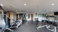 This fitness center on Plum Nelly Circle in Nashville, Tennessee, offers a well-organized and fully equipped workout facility designed to accommodate a variety of exercise routines. The single-floor layout features durable rubber flooring throughout, providing a safe and functional surface for all types of training activities.

The space is divided into distinct workout zones. The cardio area is lined with multiple treadmills and an elliptical machine positioned along a row of windows that allow natural light to fill the room and provide views of an adjacent outdoor patio area. A wall-mounted television accompanies this section, enhancing the cardio experience. The walls feature a distinctive blue and yellow horizontal stripe accent that adds a vibrant, energetic character to the space.

The strength training area includes a multi-station cable machine, adjustable weight bench, leg press machine, and a well-stocked dumbbell rack offering a range of free weights. Additional accessories such as exercise balls, yoga mats, and foam rollers are available for stretching and functional fitness. Recessed lighting and ceiling fans ensure the space remains well-lit and comfortable. A bulletin board with posted guidelines and informational signage keeps users informed. A glass door connects the fitness center to an adjacent community area, adding convenience and connectivity to the overall facility.