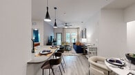 This single-story residence offers a well-designed open-concept layout finished with light wood-style flooring and neutral tones that connect each living area seamlessly. The kitchen is outfitted with dark wood cabinetry, quartz countertops, stainless steel appliances including a full-size refrigerator and range, and a tile backsplash. A breakfast bar with pendant lighting provides casual seating and transitions naturally into the dining and living areas. The living room features a ceiling fan, textured accent wall, and multiple windows that bring in natural light and views of greenery outside. A balcony door adds outdoor access from this space.

The primary bedroom includes a bold navy accent wall, ceiling fan, and windows overlooking lush exterior views. The second bedroom features a dramatic textured wallcovering and teal drapery, lending a distinct character to the room. Both bedrooms are supported by walk-in closets with multi-tier wire shelving systems and wood-style flooring. The bathroom connects directly to a walk-in closet, enhancing functionality. Throughout the residence, black hardware accents and contemporary design details contribute to a cohesive, modern aesthetic.