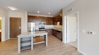 Located at 2435 NE Marshall St in Minneapolis, MN, this well-appointed single-floor residence offers a clean, modern aesthetic throughout. The open-concept living and kitchen area is bright and airy, with light-toned hardwood-style flooring and crisp white walls that maximize the sense of space. Large sliding glass doors lead to a private balcony, flooding the interior with natural light and providing outdoor views of the surrounding neighborhood.

The kitchen is a functional centerpiece, featuring rich dark wood cabinetry that extends to the ceiling for ample storage, granite countertops, a central island, and a full suite of stainless steel appliances including a refrigerator, range, microwave, and dishwasher. Recessed lighting adds a polished finish to this well-designed cooking space.

The unit includes two bathrooms: a full bath with a tub-shower combination, dark wood vanity, and light wood-style flooring, and a second bath with a single vanity, large mirror, and matching finishes. Storage is well-considered, with a generously sized walk-in closet outfitted with multi-tiered wire shelving systems and carpeted flooring. The overall design emphasizes neutral tones, clean lines, and practical finishes, creating a comfortable and functional living environment.