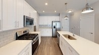 This single-floor unit presents a clean, contemporary design with a neutral color palette, dark-toned hardwood-style flooring, and white trim throughout. The kitchen serves as a standout feature, offering white shaker-style cabinetry extending to the ceiling, quartz countertops, a subway tile backsplash, and a center island with an undermount sink. Stainless steel appliances — including a gas range, microwave, refrigerator with ice maker, and dishwasher — complete the space, which is illuminated by recessed lighting and a brushed nickel pendant fixture.

The living area is open and bright, with a large sliding glass door that invites natural light and connects to the exterior. The bedrooms are well-sized, with one featuring a window with roller shades. Both are served by generous closet spaces, including a large walk-in closet equipped with multi-tiered wire shelving systems for organized storage.

Two bathrooms round out the unit. One includes a tub-shower combination with white subway tile surround, while the second features a glass-enclosed tile shower, a white vanity with quartz countertop, and a large mirror. Both bathrooms feature light tile flooring, creating a bright and clean aesthetic throughout.
