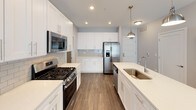 This single-floor unit presents a clean, contemporary design with a neutral color palette, dark-toned hardwood-style flooring, and white trim throughout. The kitchen serves as a standout feature, offering white shaker-style cabinetry extending to the ceiling, quartz countertops, a subway tile backsplash, and a center island with an undermount sink. Stainless steel appliances — including a gas range, microwave, refrigerator with ice maker, and dishwasher — complete the space, which is illuminated by recessed lighting and a brushed nickel pendant fixture.

The living area is open and bright, with a large sliding glass door that invites natural light and connects to the exterior. The bedrooms are well-sized, with one featuring a window with roller shades. Both are served by generous closet spaces, including a large walk-in closet equipped with multi-tiered wire shelving systems for organized storage.

Two bathrooms round out the unit. One includes a tub-shower combination with white subway tile surround, while the second features a glass-enclosed tile shower, a white vanity with quartz countertop, and a large mirror. Both bathrooms feature light tile flooring, creating a bright and clean aesthetic throughout.