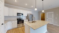 This single-floor residence offers a thoughtfully designed layout across two bedrooms and two full bathrooms. The open-concept kitchen and living area serves as the heart of the unit, featuring white shaker cabinetry, a subway tile backsplash, and stainless steel appliances including a range, microwave, and refrigerator. A central island topped with granite countertops provides additional workspace and doubles as a casual dining area, illuminated by pendant lighting overhead. Crown molding and recessed lighting add a refined touch throughout.

Light hardwood flooring runs through the kitchen, living area, and bathrooms, while the bedrooms are finished with plush carpeting. The living room benefits from a ceiling fan, crown molding, and a sliding glass door that opens to a balcony with outdoor views. The primary bedroom is generously sized and connects to a full en-suite bathroom featuring a tub-shower combination and granite vanity, with access to a walk-in closet equipped with wire shelving. The second bedroom includes a large window with exterior views. A second full bathroom mirrors similar finishes, and a dedicated laundry area completes the unit.