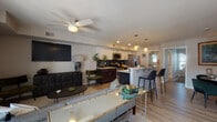 This single-floor residence offers a thoughtfully designed open-concept layout that seamlessly connects the living, dining, and kitchen areas. The living room is a comfortable and stylish space, featuring light wood-style flooring, a ceiling fan, and a wall-mounted flat-screen TV above a distinctive dark wood media console. A large statement painting adds a bold artistic touch, while natural light filters in through a nearby window.

The kitchen is well-equipped for everyday cooking, showcasing a two-tone cabinet design with white upper cabinets and dark espresso lower cabinets, complemented by a sleek dark tile backsplash and light stone countertops. Stainless steel appliances include a gas range, over-the-range microwave, and a French door refrigerator. A peninsula with seating provides a casual dining option alongside the dedicated dining area, which features a round wooden table surrounded by plush emerald green upholstered chairs.

The bedroom is a serene retreat with neutral tones, dual windows with decorative valances that allow ample natural light, a ceiling fan, and a closet with bi-fold doors. The full bathroom is clean and modern, offering a white vanity with under-mount sink, a lighted mirror, wood-look tile flooring, and a window for natural ventilation.