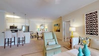 This single-floor residence in Columbus, Georgia, offers a thoughtfully designed layout that balances comfort and functionality. The open-concept living and dining area serves as the heart of the home, finished with plush carpeting, crown molding, and warm neutral tones throughout. The living room provides generous space for seating arrangements and is enhanced by natural light and stylish pendant lighting. Adjacent to it, the dining area accommodates a round table beneath a chandelier, complemented by a decorative mirror and colorful wall art.

The galley-style kitchen features white cabinetry, dark countertops, tile flooring, and stainless steel appliances, including a refrigerator, range, and dishwasher. A breakfast bar connects the kitchen to the main living space.

The bedroom is carpeted and tranquil, with crown molding and direct sightlines to the main living area. A walk-in closet with wire shelving provides generous storage. The bathroom offers tile flooring, a vanity with white cabinetry, and well-lit mirrors.

A dedicated laundry area houses a full-size washer and dryer. The overall ambiance is bright, clean, and cohesive, with a neutral palette accented by teal and gold tones.
