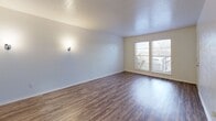 Located in Dallas, TX, this one-bedroom, two-bathroom unit offers a practical and well-organized single-floor layout. Wood-look flooring runs throughout, providing a clean, cohesive look across all living areas. The combined dining and living room is bright and open, benefiting from large windows that invite natural light and offer outdoor views. Wall sconces add a warm accent to the main living space.

The kitchen features warm-toned wood cabinetry, white appliances including a range and refrigerator, and a pass-through counter that connects it to the living area — promoting an open feel while maintaining functional separation. Built-in shelving adjacent to the pass-through adds additional display or storage space. Two pantries provide ample storage capacity, a notable convenience for the unit's scale.

The bedroom is a comfortable, well-proportioned space equipped with a ceiling fan with light fixture and a window for natural light. A dedicated closet with a hanging rod offers straightforward storage. The textured ceilings in the living areas and smooth walls throughout contribute to the unit's clean aesthetic.

Both bathrooms are finished with white tile surround tub/shower combinations and chrome fixtures, maintaining a crisp, functional appearance. Overall, the unit presents an efficient and neatly designed living space suited for everyday comfort.