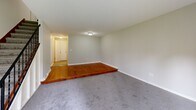 Located at 128 W Pleasant St in Manlius, NY, this multi-floor home offers two bedrooms, two bathrooms, and a finished basement across three levels. The main living area is a generously sized, carpet-floored room filled with natural light, featuring a sliding glass door that opens to an outdoor patio area with green lawn views. A wall-mounted air conditioning unit provides climate control. The kitchen is efficiently laid out with warm oak cabinetry, granite-style countertops, tile flooring, a gas range, and a full-size refrigerator — offering ample storage and functionality. Both bathrooms are cleanly finished, with one featuring a full tub-shower combo, white vanity, and tile flooring. The two bedrooms are carpeted and neutral-toned; the spacious primary bedroom includes a closet, while the second bedroom benefits from natural light through a window with blinds. A distinctive feature of the living space is a raised hardwood platform that transitions to carpeted areas, adding architectural interest. The basement level provides considerable utility space with an exposed ceiling, painted concrete block walls, and an in-unit washer and dryer. A staircase connects all floors, and a hallway provides smooth flow throughout the home.