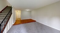 Located at 128 W Pleasant St in Manlius, NY, this multi-floor home offers two bedrooms, two bathrooms, and a finished basement across three levels. The main living area is a generously sized, carpet-floored room filled with natural light, featuring a sliding glass door that opens to an outdoor patio area with green lawn views. A wall-mounted air conditioning unit provides climate control. The kitchen is efficiently laid out with warm oak cabinetry, granite-style countertops, tile flooring, a gas range, and a full-size refrigerator — offering ample storage and functionality. Both bathrooms are cleanly finished, with one featuring a full tub-shower combo, white vanity, and tile flooring. The two bedrooms are carpeted and neutral-toned; the spacious primary bedroom includes a closet, while the second bedroom benefits from natural light through a window with blinds. A distinctive feature of the living space is a raised hardwood platform that transitions to carpeted areas, adding architectural interest. The basement level provides considerable utility space with an exposed ceiling, painted concrete block walls, and an in-unit washer and dryer. A staircase connects all floors, and a hallway provides smooth flow throughout the home.