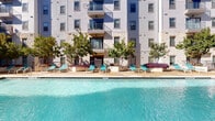 Located in Austin, TX 78731, this residential community showcases thoughtfully designed outdoor amenities that blend natural landscaping with functional gathering spaces. At the heart of the community is a sparkling resort-style swimming pool, framed by a limestone-accented building facade and surrounded by lounge chairs, making it an ideal spot for relaxation and recreation under the Texas sun. Balconied upper floors overlook the pool area, adding an architectural sense of depth and vertical presence.

Beyond the pool, the property features a series of serene courtyard spaces characterized by manicured lawns, concrete stepping stone pathways, and a linear water channel feature accented with smooth river rocks — offering a calming, meditative ambiance. Adirondack-style chairs are positioned throughout the outdoor areas, inviting residents to unwind in a tranquil setting.

Lush greenery is a defining element of the community, with mature oak trees providing generous shade, vine-covered pergola structures, ornamental grasses, flowering shrubs, and neatly trimmed hedgerows. The landscaping creates a layered, park-like environment that softens the built architecture throughout. The overall outdoor design reflects a commitment to creating comfortable, well-appointed communal spaces suited for Austin's vibrant, outdoor-oriented lifestyle.