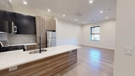 Located at 586 Central Avenue in East Orange, NJ, this thoughtfully designed one-bedroom, one-bathroom unit offers a modern living experience with a clean, contemporary aesthetic throughout. Light hardwood flooring flows seamlessly across the open-concept living and dining area, which is bathed in natural light from sleek, black-framed windows. Recessed lighting overhead adds a polished, well-lit ambiance throughout the space.

The standout kitchen features a large central island with a white quartz countertop, an under-mount sink with a matte black faucet, and built-in open shelving below. Cabinetry combines dark upper cabinets with warm wood-toned lower units, complemented by a tiled backsplash and a full suite of stainless steel appliances, including a gas range, microwave, and refrigerator. The kitchen transitions effortlessly into the living and dining area, making it ideal for entertaining.

The spacious primary bedroom offers a tranquil retreat with hardwood flooring, a window with outdoor views, and access to multiple closets, providing generous storage. The bathroom is finished with clean white subway tile, large-format floor tiles, matte black fixtures, and a shower-tub combination. An in-unit laundry area and five closets throughout round out this well-appointed home.
