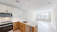 Located at 200 Middletown Blvd in Langhorne, PA, this thoughtfully designed two-bedroom, one-bathroom residence offers a clean, contemporary aesthetic across a well-organized single floor. The open-concept kitchen and living area serves as the heart of the home, showcasing a two-tone cabinetry design with warm wood lower cabinets and crisp white uppers, complemented by quartz countertops and a peninsula with an undermount sink. Stainless steel appliances, including a French door refrigerator, electric range, over-the-range microwave, and dishwasher, complete the modern kitchen. Elegant pendant lighting adds a refined touch overhead. The adjacent living room is bathed in natural light from a large multi-pane window, with light wood-style flooring flowing throughout the main areas. Both bedrooms feature neutral wall tones, plush carpet, and generous windows fitted with blinds that allow ample sunlight. The full bathroom is finished with large-format tile flooring, a wood-toned vanity with quartz countertop, and clean white shaker-style doors. A dedicated laundry room with side-by-side Whirlpool washer and dryer adds everyday convenience. Hallways and a closet provide practical storage throughout the residence.