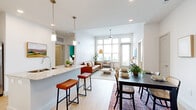 This thoughtfully designed 2-bedroom, 2-bathroom residence combines modern aesthetics with functional living across a single floor. The open-concept living, dining, and kitchen area serves as the heart of the home, featuring light hardwood flooring and an abundance of natural light streaming through oversized windows with outdoor views. The kitchen is appointed with white shaker cabinetry, granite countertops, stainless steel appliances, a built-in wine rack, and a central island with bar seating illuminated by pendant lighting. The dining area accommodates a full table and flows seamlessly into the bright living room, which features a textured accent wall and ceiling fan. The primary bedroom is a well-proportioned retreat highlighted by a bold teal accent wall, large window, and light wood flooring. Its en-suite bathroom includes a double-sink vanity with granite countertops, white cabinetry, and a marble-tiled soaking tub. The second bedroom shares the home's clean, modern palette. Two dedicated closets provide ample storage throughout. The overall ambiance is bright, airy, and contemporary, with consistent finishes that lend a cohesive and polished character to every room.
