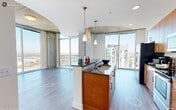 This contemporary high-rise residence offers a striking blend of industrial and modern design elements across a single thoughtfully laid-out floor. Exposed concrete columns and ceilings contrast beautifully with crisp white walls and light wood-tone flooring, creating an urban aesthetic throughout the living spaces. Floor-to-ceiling windows flood the interior with abundant natural light and frame panoramic city skyline views from multiple rooms, including the living area and bedrooms. A private balcony extends the living space outdoors, offering an elevated vantage point over the surrounding cityscape. The kitchen is well-appointed with warm wood cabinetry extending to the ceiling, stainless steel appliances including a side-by-side refrigerator, range, and microwave, dark granite countertops, and a breakfast bar with pendant lighting. The bedrooms feature plush carpet flooring and their own large windows overlooking the city below. The bathrooms are finished with tile flooring, granite-topped wood vanities, and a tub-shower combination. A curved architectural detail in the entryway corridor adds a distinctive design touch. The unit also includes in-unit laundry. Throughout, the residence balances refined finishes with bold structural elements for a sophisticated urban living experience.