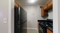 Located at 110 North 17th Street in St. Louis, Missouri, this compact single-floor unit makes efficient use of its space across a living room, kitchen, bathroom, and two hallways. The living room is the largest area of the unit, featuring light-toned hardwood-style flooring, neutral taupe walls, and clean white trim. A large window dressed with vertical blinds allows generous natural light to fill the room, creating an open and airy feel. A wall-mounted HVAC unit sits beneath the window, providing in-unit climate control. The galley-style kitchen is efficiently laid out with warm wood cabinetry, dark granite countertops, and black appliances including a gas range and a full-size refrigerator. Light hardwood-style flooring continues into this space, and overhead cabinetry provides ample storage. The bathroom features large-format tile flooring in a neutral gray tone, a pedestal sink, a standard toilet, and an over-toilet wood-toned cabinet for additional storage. A vanity light fixture above the mirror provides bright, functional illumination. Two hallways connect the rooms, maintaining a straightforward and practical flow throughout the unit. Overall, the space presents a clean, functional layout well-suited for single occupancy.