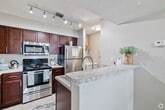 This 730-square-foot, single-floor unit at 5455 Caribe Court in Virginia Beach, VA offers a practical and comfortable layout across two bedrooms, two bathrooms, two closets, and a combined kitchen and living room. The living room serves as the heart of the unit, featuring light hardwood-style flooring, a tile-surround wood-burning fireplace, a ceiling fan, and a sliding glass door that opens to a private balcony with lush, tree-lined views. The galley-style kitchen is well-appointed with white shaker cabinetry, dark granite countertops, subway tile backsplash, stainless steel appliances including a refrigerator and over-the-range microwave, and durable hardwood-style flooring. Both bedrooms are carpeted and finished in neutral tones, with windows that bring in natural light and views of surrounding greenery. The primary bedroom measures 170 square feet and includes closet access. Both bathrooms feature tub/shower combinations with clean, white surrounds. A connecting hallway ties the private areas of the unit together, completing this efficient and well-maintained floor plan.