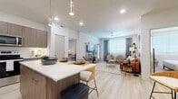 This single-floor residence is thoughtfully designed with a contemporary aesthetic, combining functionality and style across its well-organized layout. The open-concept kitchen serves as a central hub, featuring flat-panel wood-toned cabinetry, a subway tile backsplash, stainless steel appliances, and a generous island with seating for three — illuminated by elegant pendant lighting overhead. Light wood-style flooring runs consistently throughout, lending the space a cohesive, airy feel.

The kitchen flows seamlessly into the living area, where a ceiling fan overhead and a large window with blinds and drape panels allow for natural light and comfortable airflow. The living room provides ample space for lounging and entertaining.

Two bedrooms are present, each benefiting from natural light through generously sized windows. One bedroom includes light wood flooring and a compact workspace, while the primary bedroom features soft carpeting, a ceiling fan, and sufficient space for a full furniture arrangement.

The bathroom is well-appointed with wood-toned vanity cabinetry, a white quartz countertop, a full-size soaking tub with shower, and direct access to the adjacent bedroom. A separate closet provides convenient built-in storage. The overall ambiance is clean, modern, and welcoming.