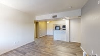 This single-floor residence offers a clean, functional layout with a cohesive neutral color palette and wood-look flooring that flows consistently throughout the space. The open living area is bright and welcoming, with light-toned walls, a ceiling fan, and a seamless connection to the kitchen via a peninsula-style pass-through that enhances the sense of openness. Natural light enters through windows near the entry, which features a front door flanked by vertical-blind-covered sidelights. The galley kitchen is well-equipped with gray cabinetry, light speckled countertops, a double stainless steel sink, and black appliances including a gas range, over-the-range microwave, dishwasher, and refrigerator. A separate pantry or utility closet adds practical storage. The bedrooms are generously sized with the same warm wood-look flooring, clean white walls, and ample wall space. The bathrooms feature white vanity cabinetry topped with light speckled countertops, undermount oval sinks with brushed nickel faucets, large wall mirrors, and shower-tub combinations. Central HVAC vents are present throughout, ensuring year-round climate control. Overall, the space presents a tidy, move-in-ready environment with a straightforward and practical design.