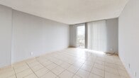 Located at 14795 NE 18th Ave in North Miami, FL, this 2-bedroom, 1-bathroom unit offers a straightforward, functional layout across a single floor. Light-toned ceramic tile flooring runs consistently throughout every room, contributing to a clean, cohesive aesthetic.

The living room is the largest area of the unit, featuring a built-in niche along one wall and a floor-to-ceiling sliding glass door that opens to an outdoor view of the surrounding North Miami cityscape, allowing substantial natural light to fill the space. A second open area adjacent to the living room includes another built-in niche and flush ceiling lighting.

The primary bedroom is a generously sized room featuring dual closets and large corner windows on two walls, providing panoramic outdoor views and ample natural light. The second bedroom is a well-proportioned room with its own window offering exterior views and access to closet storage.

Two hallways connect the rooms efficiently throughout the unit. The bathroom includes a full tub-shower combination finished with large-format beige ceramic wall tiles and chrome fixtures, maintaining the neutral palette found throughout the unit. Overall, the space presents a clean, minimalist character well-suited to the South Florida climate.