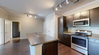 This single-floor residence offers a thoughtfully designed layout that balances functionality and modern style. The kitchen serves as the centerpiece of the home, showcasing rich dark espresso cabinetry that extends to the ceiling for ample storage, complemented by stainless steel appliances including a gas range, over-the-range microwave, and refrigerator. A peninsula with a double stainless steel sink and granite-style countertops provides additional workspace and creates a natural division between the kitchen and the adjoining living area. Track lighting illuminates the kitchen, while crown molding adds a refined architectural detail throughout. Rich hardwood-style flooring runs through the main living and kitchen areas, lending warmth and continuity to the space. The living area is generously proportioned, featuring a ceiling fan and access to natural light through a large window with outdoor views. The carpeted bedroom offers a quiet retreat, also equipped with a ceiling fan for comfort. The bathroom is well-sized, featuring dark cabinetry with matching hardware, a granite-style vanity countertop, a full tub-shower combination with tile surround, and durable stone-look tile flooring. A large double-door closet provides substantial storage. The overall ambiance is clean, contemporary, and move-in ready.