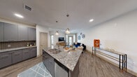 This 1-bedroom, 1-bathroom unit offers a thoughtfully designed open-concept layout across a single floor. The kitchen serves as a central hub, showcasing granite countertops on a large island with a double sink, gray cabinetry, a mosaic tile backsplash, stainless steel appliances, and stylish pendant lighting. The island flows seamlessly into the living area, which features wood-style flooring, a ceiling fan, and access to natural light through large windows and a glass door that opens to an outdoor space. The bedroom is a comfortable retreat with plush carpeting, multiple windows allowing ample natural light, and a ceiling fan. It connects to a generously sized walk-in closet outfitted with wrap-around shelving and dedicated hanging rods. The bathroom is finished with granite countertops, gray cabinetry, a large vanity mirror, and a full tub-shower combination. A dedicated laundry room houses a full-size washer and offers additional built-in shelving for extra storage. Recessed lighting and a neutral color palette throughout lend the space a clean, modern aesthetic.