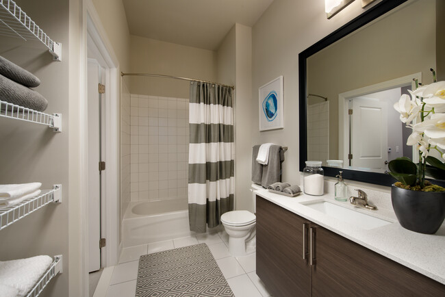 Bathroom with storage space, tile floor, European-style cabinetry, white countertop, shower with tile backsplash and hard surface flooring - Avalon Dunn Loring