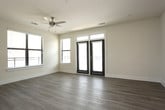 This single-floor residence offers a thoughtfully designed layout with a clean, modern aesthetic throughout. The open-concept living and kitchen area serves as the heart of the space, featuring light-toned hardwood-style flooring, neutral walls, and generous natural light streaming through large windows and glass-panel doors that provide outdoor access. The kitchen is well-equipped with dark taupe cabinetry, a classic subway tile backsplash, granite countertops, stainless steel appliances, and a central island with built-in shelving — illuminated by stylish pendant lights and a track lighting system above. The adjoining living area is spacious and open, with ample room for a variety of furniture arrangements. The bedrooms are finished with plush carpeting, ceiling fans with light fixtures, and windows fitted with blinds for natural light control. Each bedroom includes convenient closet access. A dedicated bedroom features a walk-in closet visible through a dark-paneled interior door. The bathrooms are finished with tile flooring, granite-topped vanities with undermount sinks, and a tiled tub-shower combination. A hallway utility area accommodates an in-unit washer, adding everyday convenience. Throughout, dark interior doors provide a striking contrast against the light walls and flooring.