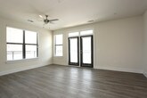 This single-floor residence offers a thoughtfully designed layout with a clean, modern aesthetic throughout. The open-concept living and kitchen area serves as the heart of the space, featuring light-toned hardwood-style flooring, neutral walls, and generous natural light streaming through large windows and glass-panel doors that provide outdoor access. The kitchen is well-equipped with dark taupe cabinetry, a classic subway tile backsplash, granite countertops, stainless steel appliances, and a central island with built-in shelving — illuminated by stylish pendant lights and a track lighting system above. The adjoining living area is spacious and open, with ample room for a variety of furniture arrangements. The bedrooms are finished with plush carpeting, ceiling fans with light fixtures, and windows fitted with blinds for natural light control. Each bedroom includes convenient closet access. A dedicated bedroom features a walk-in closet visible through a dark-paneled interior door. The bathrooms are finished with tile flooring, granite-topped vanities with undermount sinks, and a tiled tub-shower combination. A hallway utility area accommodates an in-unit washer, adding everyday convenience. Throughout, dark interior doors provide a striking contrast against the light walls and flooring.