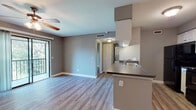 This single-floor residence offers a cohesive and modern layout designed for comfortable everyday living. Throughout the space, light wood-style vinyl flooring provides a clean, uniform aesthetic that ties each room together seamlessly.

The open-concept living area is bright and welcoming, featuring a ceiling fan with integrated lighting and a sliding glass door that opens to a private balcony, allowing natural light to pour in and offering views of the surrounding outdoors. The living space flows directly into the kitchen and dining area, creating an interconnected environment ideal for both relaxing and entertaining.

The kitchen is efficiently designed with white cabinetry, dark granite-style countertops, and a full suite of black appliances including a refrigerator, electric range, microwave, and dishwasher. A peninsula with a built-in sink provides additional counter space and serves as a natural divider between the kitchen and the adjoining areas. A louvered closet door within the kitchen offers convenient pantry or storage access.

The bedroom is a generously sized, quiet retreat with neutral gray walls, a large window fitted with blinds that admits ample natural light, and easy access to the bathroom. The bathroom is clean and functional, featuring a tiled shower/tub combination, wood-style flooring, and a louvered closet for storage. The overall palette of warm grays and whites gives the entire space a fresh, move-in-ready appeal.