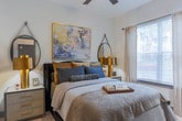 Located on Abernathy Road NE in Sandy Springs, Georgia, this thoughtfully designed single-floor residence combines contemporary style with functional living. The open-concept layout seamlessly connects the living, dining, and kitchen areas, creating an inviting and cohesive space.

The living room is anchored by a tufted sofa, a rich wood coffee table, and a bold slate-blue accent wall adorned with abstract artwork. A striking sputnik chandelier and large floor-to-ceiling windows flood the space with natural light, while warm hardwood flooring runs throughout the main living areas.

The kitchen is outfitted with white shaker cabinetry, granite countertops, a classic subway tile backsplash, stainless steel appliances, and a peninsula with bar seating — ideal for casual dining and entertaining.

The primary bedroom offers a serene retreat, bathed in natural light from oversized windows and finished with plush carpeting. A second bedroom provides a cozy, well-lit space with ample room for furnishings.

The bathroom features a long double-vanity with white cabinetry and black hardware, grey tile flooring, a walk-in glass-enclosed shower, and elegant runner accents — delivering a clean, spa-inspired aesthetic throughout.