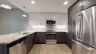 This single-floor residence showcases a thoughtfully designed layout that balances modern finishes with functional living spaces. The kitchen serves as a standout feature, boasting a two-tone cabinet scheme that pairs crisp white upper cabinets with dark wood-grain lower cabinets. Granite countertops, a penny-tile backsplash with under-cabinet lighting, and a full suite of stainless steel appliances—including a range, microwave, dishwasher, and refrigerator—complete the space. Light wood-style flooring runs throughout the kitchen and living areas, contributing to a warm, cohesive aesthetic.

The open living area benefits from natural light through white-trimmed windows and flows seamlessly toward the kitchen. The bedroom features plush wall-to-wall carpeting, dual closets with paneled doors, and corner windows that invite natural light. Neutral taupe tones throughout create a calm, welcoming atmosphere.

The bathroom is finished with large-format tile flooring, a dark wood vanity with a stone-topped countertop, and a glass-enclosed shower. An in-unit laundry area accommodates a stacked washer and dryer, adding everyday convenience to this well-appointed residence.