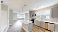 Located at Petty Road in Durham, NC, this single-floor residence offers a thoughtfully designed open-concept layout that maximizes functionality and comfort. The combined kitchen and living area serves as the heart of the home, featuring warm hardwood-style flooring, soft neutral walls, and large windows that flood the space with natural light. The kitchen is outfitted with gray shaker-style cabinetry, a subway tile backsplash, white quartz countertops, and a full suite of stainless steel appliances including a refrigerator, range, microwave, and dishwasher. A central island with pendant lighting provides additional prep space and casual seating. The living area extends naturally from the kitchen, with a ceiling fan and views to the outdoors. The bedroom is a comfortable retreat with plush carpeting, a ceiling fan, and generously sized windows overlooking the surrounding neighborhood. Two closets provide ample storage. The bathroom features large-format tile flooring, a glass-enclosed walk-in shower, and clean white fixtures. The overall design palette — neutral tones, modern hardware, and consistent finishes — creates a cohesive, move-in-ready living environment.