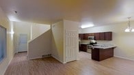 This two-story residence offers a well-designed layout that balances functionality and comfort across both levels. The main floor features an open-concept living and kitchen area unified by warm light hardwood flooring that extends throughout the space. The kitchen is outfitted with rich dark wood cabinetry, stainless steel appliances including a microwave, electric range, and refrigerator, as well as a dark-toned island that provides additional prep and storage space. A recessed overhead light fixture brightens the kitchen area, while neutral beige walls create a clean, welcoming backdrop. A six-panel interior door provides access to additional utility or storage areas adjacent to the kitchen. A staircase with clean white risers leads to the second floor, making the transition between levels both practical and visually open. Floor vents are integrated into the layout, indicating a central HVAC system for year-round climate control. The overall design aesthetic is understated and move-in ready, with neutral finishes that allow for easy personalization. The combination of modern appliances, ample cabinetry, and cohesive flooring makes this a highly functional and comfortable multi-level home.