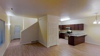 This two-story residence offers a well-designed layout that balances functionality and comfort across both levels. The main floor features an open-concept living and kitchen area unified by warm light hardwood flooring that extends throughout the space. The kitchen is outfitted with rich dark wood cabinetry, stainless steel appliances including a microwave, electric range, and refrigerator, as well as a dark-toned island that provides additional prep and storage space. A recessed overhead light fixture brightens the kitchen area, while neutral beige walls create a clean, welcoming backdrop. A six-panel interior door provides access to additional utility or storage areas adjacent to the kitchen. A staircase with clean white risers leads to the second floor, making the transition between levels both practical and visually open. Floor vents are integrated into the layout, indicating a central HVAC system for year-round climate control. The overall design aesthetic is understated and move-in ready, with neutral finishes that allow for easy personalization. The combination of modern appliances, ample cabinetry, and cohesive flooring makes this a highly functional and comfortable multi-level home.