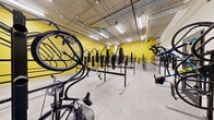 Located at 311 N Willson Ave in Bozeman, Montana, this dedicated bike room is a well-organized, purpose-built facility designed to accommodate a large number of bicycles efficiently. The space features a generous open floor plan with a polished concrete floor that provides a clean, durable surface throughout.

The room is immediately distinguished by its bold yellow accent walls, which create a vibrant, energetic atmosphere and contrast sharply with the exposed concrete structural columns and walls that line portions of the perimeter. The ceiling is left exposed, revealing overhead ductwork, conduit runs, and fluorescent strip lighting that ensures the space is evenly and brightly illuminated.

The primary feature of the room is its extensive system of black steel bicycle racks. Both freestanding floor-mounted racks and wall-mounted rack systems are installed throughout, offering flexible and high-capacity storage for a wide variety of bicycle types. The racks are arranged in organized rows, maximizing the use of available floor space while maintaining clear circulation paths between them.

A wall-mounted heater is visible, providing climate control during Bozeman's cold winters. The room is accessed through a dedicated door, ensuring secure and controlled entry. Overall, this bike room delivers a functional, well-equipped, and visually distinctive storage solution for cyclists.