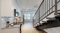 Located on E Adams Street in the heart of downtown Jacksonville, Florida, this two-story, one-bedroom, two-bathroom residence offers a well-organized layout spread across two evenly sized floors. The ground floor features hardwood-style flooring throughout, setting a warm and modern tone. A dedicated laundry room houses a stacked washer and dryer unit, providing everyday convenience. Two full bathrooms are finished with granite-topped white vanities, sleek rectangular mirrors, and brushed nickel fixtures. One bathroom includes a tiled soaking tub and shower combination, while the other serves as an en-suite accessible from the bedroom. The upper floor is home to the generously sized primary bedroom, which stands out with its exposed concrete ceiling — a striking industrial design element — paired with a ceiling fan and plush wall-to-wall carpeting. Multiple windows flood the room with natural light and offer views of the surrounding urban neighborhood. A dedicated walk-in closet fitted with wire shelving and carpeted flooring provides ample storage. The staircase connecting the two floors features a dark handrail that contrasts neatly with the light-toned walls and carpet. Throughout the residence, a neutral gray and white palette creates a clean, contemporary ambiance well-suited to urban living.