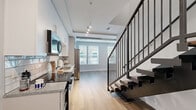 Located on E Adams Street in the heart of downtown Jacksonville, Florida, this two-story, one-bedroom, two-bathroom residence offers a well-organized layout spread across two evenly sized floors. The ground floor features hardwood-style flooring throughout, setting a warm and modern tone. A dedicated laundry room houses a stacked washer and dryer unit, providing everyday convenience. Two full bathrooms are finished with granite-topped white vanities, sleek rectangular mirrors, and brushed nickel fixtures. One bathroom includes a tiled soaking tub and shower combination, while the other serves as an en-suite accessible from the bedroom. The upper floor is home to the generously sized primary bedroom, which stands out with its exposed concrete ceiling — a striking industrial design element — paired with a ceiling fan and plush wall-to-wall carpeting. Multiple windows flood the room with natural light and offer views of the surrounding urban neighborhood. A dedicated walk-in closet fitted with wire shelving and carpeted flooring provides ample storage. The staircase connecting the two floors features a dark handrail that contrasts neatly with the light-toned walls and carpet. Throughout the residence, a neutral gray and white palette creates a clean, contemporary ambiance well-suited to urban living.
