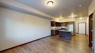 Located at 14500 51st Ave NE in Marysville, Washington, this two-bedroom, one-bathroom residence offers a thoughtfully designed single-floor layout. The kitchen serves as a standout feature, outfitted with rich dark wood cabinetry, light quartz-style countertops, a mosaic tile backsplash, and a full suite of stainless steel appliances including a range, microwave, and refrigerator. A central kitchen island provides additional prep and dining space. Warm wood-look flooring runs through the kitchen and main areas, lending a cohesive and clean aesthetic throughout. The living area is carpeted and open, with direct sightlines into the kitchen for a connected feel. Both bedrooms are carpeted and filled with natural light from windows overlooking greenery. The primary bedroom connects to a spacious walk-in closet equipped with wire shelving for ample storage. The bathroom features a dark wood vanity with a light countertop and wood-look flooring, and notably includes a stacked washer and dryer unit, adding everyday convenience. Neutral wall tones and consistent finishes throughout create a calm, move-in-ready environment well-suited for comfortable residential living.