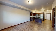Located at 14500 51st Ave NE in Marysville, Washington, this two-bedroom, one-bathroom residence offers a thoughtfully designed single-floor layout. The kitchen serves as a standout feature, outfitted with rich dark wood cabinetry, light quartz-style countertops, a mosaic tile backsplash, and a full suite of stainless steel appliances including a range, microwave, and refrigerator. A central kitchen island provides additional prep and dining space. Warm wood-look flooring runs through the kitchen and main areas, lending a cohesive and clean aesthetic throughout. The living area is carpeted and open, with direct sightlines into the kitchen for a connected feel. Both bedrooms are carpeted and filled with natural light from windows overlooking greenery. The primary bedroom connects to a spacious walk-in closet equipped with wire shelving for ample storage. The bathroom features a dark wood vanity with a light countertop and wood-look flooring, and notably includes a stacked washer and dryer unit, adding everyday convenience. Neutral wall tones and consistent finishes throughout create a calm, move-in-ready environment well-suited for comfortable residential living.