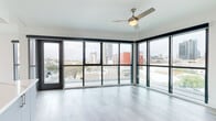 Located in the heart of San Diego at 1509 Broadway, this modern 2-bedroom, 2-bathroom residence offers a thoughtfully designed single-floor layout with contemporary finishes throughout. The open-concept living and kitchen area is a standout centerpiece, anchored by expansive floor-to-ceiling windows and sliding glass doors that flood the space with natural light and frame sweeping views of the San Diego skyline. A ceiling fan adds both style and comfort to this bright, airy living area. The kitchen is well-appointed with sleek gray cabinetry, stainless steel appliances, a subway tile backsplash, and a generous island with quartz countertops and built-in shelving — ideal for both cooking and entertaining. Light wood-style flooring flows seamlessly throughout the residence. The primary bedroom is spacious, featuring direct access to the wraparound windows and a walk-in closet. The second bedroom is bright with a large window and a charming barn-style sliding door. The primary bathroom is elegantly finished with a marble-surround walk-in shower, a large picture window, and a dual-vanity with blue-gray cabinetry. A built-in entryway nook with shelving and cabinetry provides practical storage. This residence combines urban convenience with modern design in one of San Diego's most vibrant neighborhoods.
