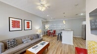 Located at 1699 Chatham Pkwy in Savannah, Georgia, this single-floor, 2-bedroom, 2-bathroom residence offers a thoughtfully designed layout with consistent hardwood-style flooring and crown molding throughout. The open-concept living, dining, and kitchen area forms the heart of the home, filled with natural light from large windows fitted with blinds. The living room features a ceiling fan, neutral gray walls, and ample space for comfortable seating. The adjacent dining area is distinguished by a charming decorative wall display, adding a unique artistic touch. The kitchen is well-equipped with stainless steel appliances, white shaker cabinetry, granite countertops, a built-in wine rack, and a peninsula with bar seating that connects seamlessly to the living space. The primary bedroom offers a serene retreat with soft blue accent walls, a ceiling fan, and a sun-facing window with outdoor views. The second bedroom echoes the calming aesthetic with similarly toned walls and generous natural light. Both bathrooms feature warm wood vanities with granite counters, tub-shower combos, and natural light from windows. The overall ambiance is bright, modern, and inviting, combining functional design with tasteful décor choices throughout.