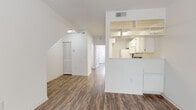 This two-story residence is thoughtfully designed with a clean, neutral palette and functional layout across both levels. The main floor features an open living and dining area finished with durable wood-look flooring that extends throughout the common spaces. A half-wall pass-through connects the living area to the kitchen, which is equipped with white cabinetry, a full suite of white appliances including a refrigerator, electric range, built-in microwave, and dishwasher, along with ample counter and storage space. Open shelving built into the pass-through wall adds a decorative yet practical touch. A hallway on the main level leads to additional rooms and a full bathroom featuring a single-sink vanity with white cabinetry and a shower-tub combination. A dedicated laundry closet houses a stacked washer and dryer unit, adding everyday convenience. The staircase leads to the upper level, where the bedrooms are finished with plush carpeting for added comfort. The primary bedroom is generously proportioned and features a walk-in closet with built-in shelving and a hanging rod, alongside a private bathroom with a vanity, mirror, and toilet. Additional bedrooms offer ceiling fans and ample natural light. Louvered closet doors and angled ceilings on the upper level add architectural character to this well-appointed home.