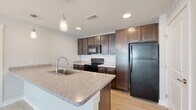 This single-floor, 3-bedroom, 2-bathroom residence offers a thoughtfully designed layout that balances comfort and functionality. The kitchen serves as a standout feature, showcasing rich dark-brown shaker-style cabinetry, speckled granite countertops, a central island with a stainless steel sink, pendant lighting, and black appliances including a refrigerator, electric range, and built-in microwave. Light wood-look flooring runs throughout the kitchen and common areas, lending a clean, contemporary feel to the space.

The three bedrooms are finished with plush neutral carpeting and feature natural light from well-positioned windows fitted with blinds. Ceiling fans are installed in the bedrooms for year-round comfort, and each room is complemented by dedicated closet space with built-in rods for organized storage.

The two bathrooms are finished with light wood-look tile flooring and dark-toned vanity cabinetry with white countertops. One bathroom features a tiled tub-shower combination, while the other offers a more open layout with accessibility-friendly grab bars. Hallways connect the rooms efficiently, and three closets throughout the unit provide generous storage capacity. The overall aesthetic is clean, modern, and move-in ready.