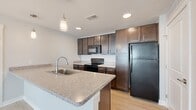 This single-floor, 3-bedroom, 2-bathroom residence offers a thoughtfully designed layout that balances comfort and functionality. The kitchen serves as a standout feature, showcasing rich dark-brown shaker-style cabinetry, speckled granite countertops, a central island with a stainless steel sink, pendant lighting, and black appliances including a refrigerator, electric range, and built-in microwave. Light wood-look flooring runs throughout the kitchen and common areas, lending a clean, contemporary feel to the space.

The three bedrooms are finished with plush neutral carpeting and feature natural light from well-positioned windows fitted with blinds. Ceiling fans are installed in the bedrooms for year-round comfort, and each room is complemented by dedicated closet space with built-in rods for organized storage.

The two bathrooms are finished with light wood-look tile flooring and dark-toned vanity cabinetry with white countertops. One bathroom features a tiled tub-shower combination, while the other offers a more open layout with accessibility-friendly grab bars. Hallways connect the rooms efficiently, and three closets throughout the unit provide generous storage capacity. The overall aesthetic is clean, modern, and move-in ready.