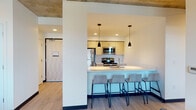 This contemporary multi-bedroom unit is thoughtfully designed for shared living, featuring a cohesive modern aesthetic carried throughout each space. The open-concept kitchen is fully equipped with stainless steel appliances—including a refrigerator, range, microwave, and dishwasher—complemented by light wood cabinetry, white quartz countertops, and a peninsula with bar seating for multiple occupants. Sleek pendant lighting in matte black adds a refined contrast to the bright, clean surfaces. Light wood-look flooring runs continuously throughout the unit, while exposed concrete ceilings lend an industrial character to the living and kitchen areas. The living room offers urban views through a large window, flooding the space with natural light, and is furnished with a leather sofa, accent chair, and a low media console. Each bedroom is efficiently arranged with a platform bed featuring under-bed storage drawers, a dedicated study desk, and a ceiling fan or window for ventilation, along with views of the surrounding cityscape. The bathrooms are finished with quartz vanity countertops, light wood cabinetry with brushed gold hardware, large wall mirrors, and sliding glass tub-shower enclosures, presenting a clean and functional design throughout.