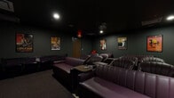 Located at 811 Grand Blvd in Kansas City, Missouri, this single-floor screening room is designed to deliver an immersive, cinema-inspired experience. The space is defined by its dark, moody aesthetic, with deep charcoal walls, black ceilings, and low ambient lighting that establish an intimate theater atmosphere throughout.

The main screening area is equipped with a large wall-mounted projection screen and ceiling-mounted projector, providing a true cinematic viewing experience. Seating consists of plush, deep burgundy leather sofas and lounge chairs arranged in a tiered, theater-style layout, offering comfortable sightlines from every position. Small side tables are positioned throughout for added convenience.

The walls are decorated with framed classic film posters — including iconic titles such as Casablanca and Gone with the Wind — reinforcing the cinematic theme and adding visual character to the space. Recessed and accent lighting provides subtle illumination without disrupting the darkened ambiance.

An adjoining anteroom or foyer area features additional décor, a red accent chair with bar-height stool, and pouf seating, creating a transitional lounge space. Carpeted flooring runs throughout, contributing to the acoustic dampening and overall warmth of the environment. The space is well-suited for private screenings, events, or gatherings.