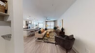 This thoughtfully designed single-floor residence offers a seamless blend of modern aesthetics and functional living. The open-concept layout connects the living, dining, and kitchen areas into one cohesive and welcoming space. The living room features wood-look flooring, a ceiling fan, and generous natural light streaming through large windows dressed with patterned curtains and blinds. The kitchen is a standout, showcasing granite countertops, a large center island with bar seating, white upper cabinetry paired with wood-toned lower cabinetry, a herringbone tile backsplash, stainless steel appliances, and elegant pendant lighting overhead. The dining area is anchored by a marble-top round table set beside bright corner windows. Two bedrooms provide comfortable retreats, each with plush carpeting, ceiling fans, large windows, and tasteful decor. The primary bathroom features a granite-topped vanity with wood cabinetry, large-format tile flooring, and a glass-enclosed shower. The secondary bathroom includes a soaking tub and shower combination with floor-to-ceiling tile surround and additional wood cabinetry storage. Throughout the residence, a consistent palette of warm neutrals and wood tones creates a cohesive, contemporary ambiance.